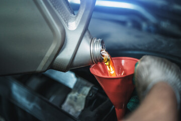 Worker pours new synthetic motor oil from canister into funnel at car service, regular oil change -...