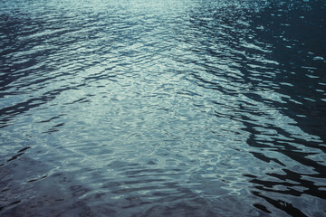 Texture of purple calm water of mountain lake. Meditative ripples on water surface. Nature minimal background of violet lake. Natural backdrop of clear dark blue water. Full frame of lake fragment.