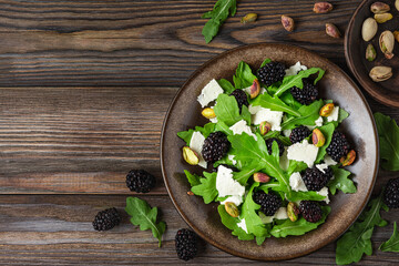 Obraz na płótnie Canvas Fresh salad with arugula, feta cheese, blackberries and pistachios in a plate on rustic wooden background