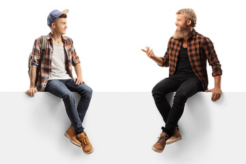 Bearded guy sitting on a white panel and talking to a young male student