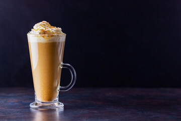 Pumpkin latte on a dark background. Pumpkin spice latte with whipped cream. Autumn drink. Minimalism. Copy space