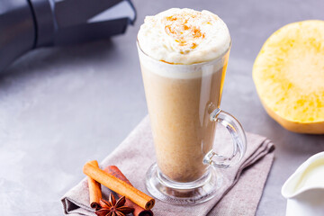 Pumpkin spice latte on a gray background. Pumpkin latte with whipped cream, coffee maker and milk jug. Hot autumn drink on cement background