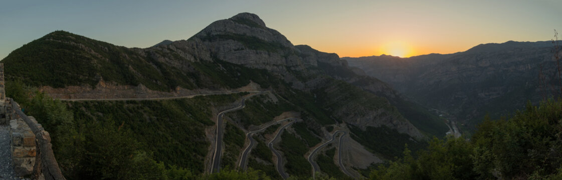 Panorama of epic roads in the north albanian mountains, famous curves and hairpin turns of SH20 road above the Cem river gorge in morning. Sun is just rising over the mountains.
