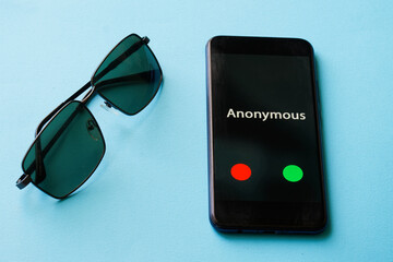 Sunglasses and smartphone with anonymous call lie on a blue surface. The problem of anonymity and espionage.