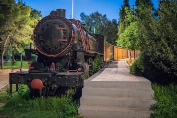 Old steam train at night parked as an outdoor exhibition of railways in a park in the greek city of Kalamata. Steam locomotive with carriages in a park on island of Peleponese