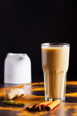 Glass of masala tea and scattered spices. Masala chai tea and milk jug on black background. Copy space