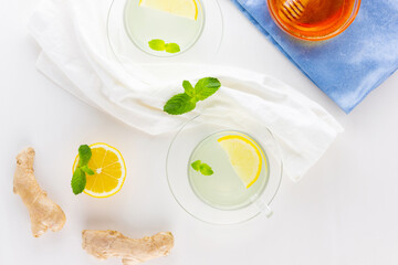 Fototapeta na wymiar Ginger tea with lemon and mint on a white napkin. Two cups of ginger tea, lemon, ginger root and honey on white background. Top view