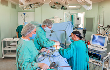 Surgeon performing cosmetic surgery on breasts in hospital operating room. Surgeon in mask wearing...