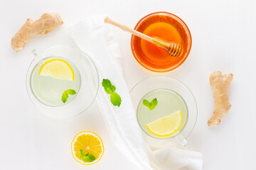 Ginger tea with lemon and mint on a white napkin. Two cups of ginger tea, lemon, ginger root and honey on white background. Top view