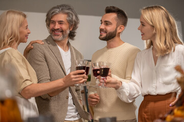 Four smiling family members in casualwear clinking with glasses of red wine