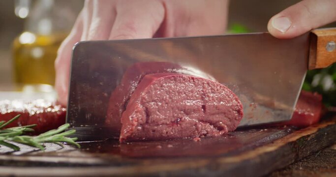 Raw liver cut into pieces with a knife on cutting board.