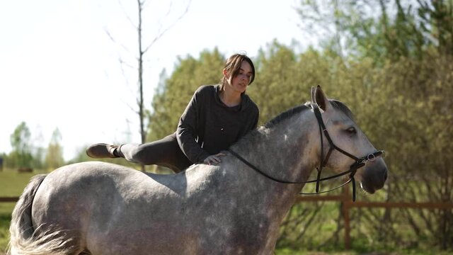 Female equestrian with long hair mounts grey horse during training