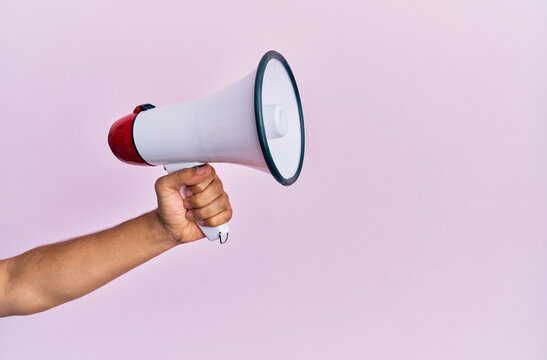 Hand of hispanic man holding megaphone over isolated pink background.