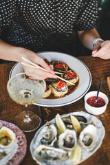 Girl eating baked susi maki with chopsticks over fresh oysters and glass of champagne on table at Japanese restaurant, top view. Japanese cuisine, fast food, seafood, fine dining concept