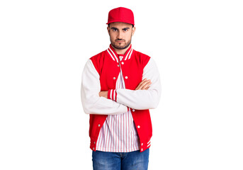 Young handsome man wearing baseball jacket and cap skeptic and nervous, disapproving expression on face with crossed arms. negative person.