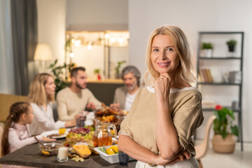 Happy mature female standing in front of camera against large family dining