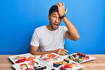 Young handsome man eating sushi sitting on the table surprised with hand on head for mistake, remember error. forgot, bad memory concept.