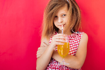 Blonde girl drinks orange juice with a straw. Copy space, isolated on pink