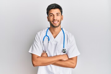 Young handsome man wearing doctor uniform and stethoscope happy face smiling with crossed arms looking at the camera. positive person.