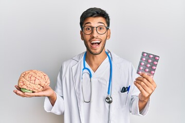 Young handsome man holding brain and pills as mental health concept celebrating crazy and amazed...