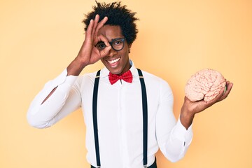 Handsome african american nerd man with afro hair holding brain smiling happy doing ok sign with...