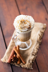 Pumpkin spice latte in a glass mug. Pumpkin latte with whipped cream and spices on a wooden background. Hot autumn coffee drink on a burlap