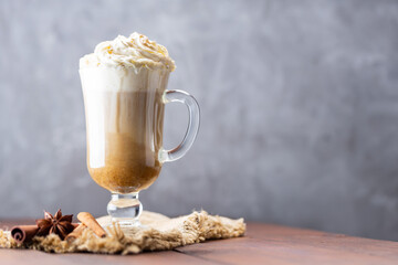 Pumpkin spice latte in a glass mug. Pumpkin latte with whipped cream and spices on a wooden background. Hot autumn coffee drink on a burlap