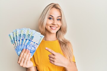 Beautiful caucasian blonde girl holding south african 100 rand banknotes smiling happy pointing with hand and finger