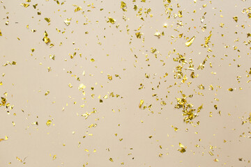 Golden confetti on beige paper trendy background. Festive holiday backdrop. Birthday congratulations Christmas New Year. Flat lay, top view, copy space.