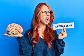 Young redhead woman holding brain and depression text angry and mad screaming frustrated and...