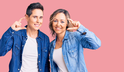 Couple of women wearing casual clothes smiling and confident gesturing with hand doing small size sign with fingers looking and the camera. measure concept.