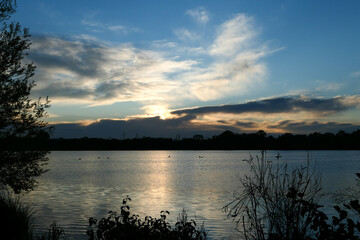 Fototapeta premium Amazing sunset over the water. Beautiful landscape with a lake and dramatic sky with cumulus clouds on the horizon.