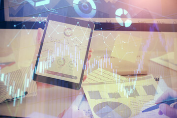 Double exposure of man's hands holding and using a digital device and forex graph drawing. Financial market concept.