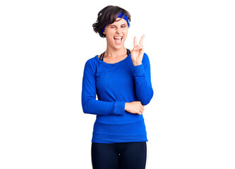 Beautiful young woman with short hair wearing training workout clothes smiling with happy face winking at the camera doing victory sign with fingers. number two.