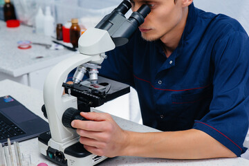 A male doctor in the laboratory studies viruses and bacteria under a microscope. Research of dangerous viruses and bacteria