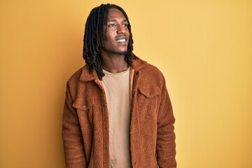 African american man with braids wearing brown retro jacket looking away to side with smile on face, natural expression. laughing confident.