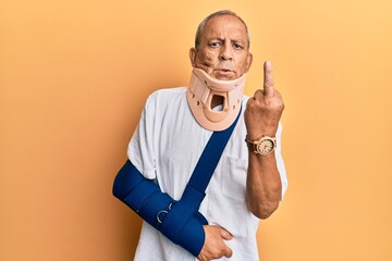 Handsome mature senior man wearing cervical collar and arm on sling showing middle finger, impolite...