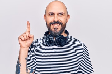 Fototapeta premium Young handsome man listening to music using headphones smiling with an idea or question pointing finger up with happy face, number one