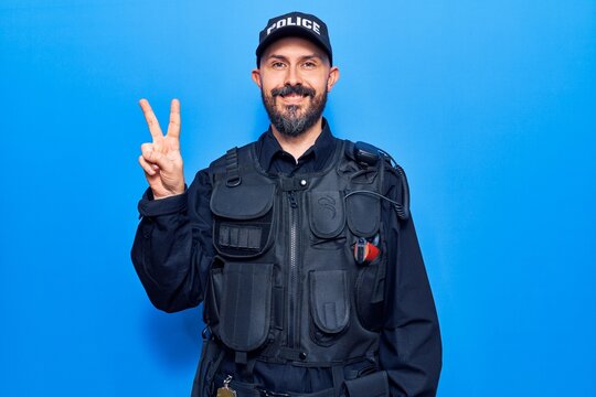 Young handsome man wearing police uniform smiling with happy face winking at the camera doing victory sign. number two.