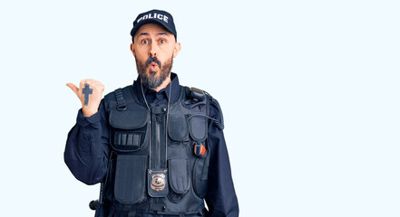 Young handsome man wearing police uniform surprised pointing with hand finger to the side, open mouth amazed expression.