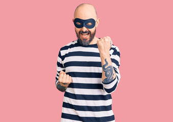 Young handsome man wearing burglar mask celebrating surprised and amazed for success with arms raised and eyes closed. winner concept.