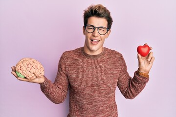 Handsome caucasian man holding brain and heart winking looking at the camera with sexy expression,...