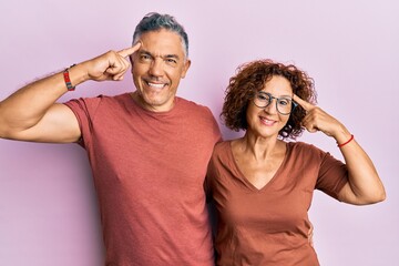 Beautiful middle age couple together wearing casual clothes smiling pointing to head with one finger, great idea or thought, good memory