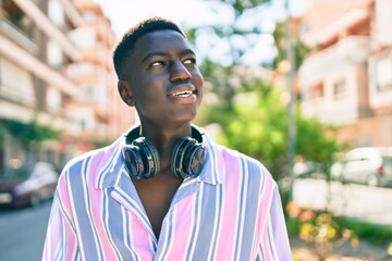 Young african american man using headphones walking at street of city.