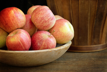Original still life photograph of a wooden bowl filled with red gala apples on wood