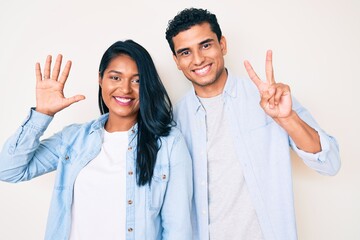 Fototapeta na wymiar Beautiful latin young couple wearing casual clothes showing and pointing up with fingers number seven while smiling confident and happy.