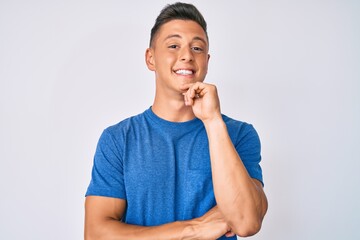 Young hispanic boy wearing casual clothes smiling looking confident at the camera with crossed arms and hand on chin. thinking positive.