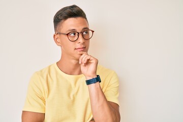 Young hispanic boy wearing casual clothes and glasses serious face thinking about question with...