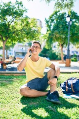 Naklejka premium Young hispanic student smiling happy using smartphone sitting on the grass at the university campus
