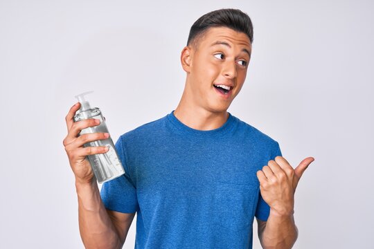 Young hispanic boy using hand sanitizer gel pointing thumb up to the side smiling happy with open mouth